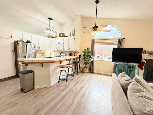 kitchen featuring tile countertops, pendant lighting, stainless steel fridge with ice dispenser, a kitchen bar, and white cabinetry