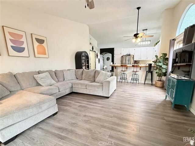 living room with light hardwood / wood-style floors, vaulted ceiling, and ceiling fan