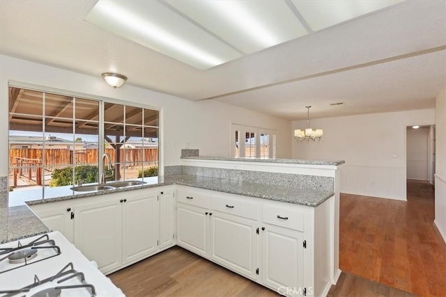 kitchen with kitchen peninsula, sink, hardwood / wood-style floors, and white cabinets