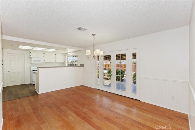 unfurnished dining area with a notable chandelier, light hardwood / wood-style floors, and a textured ceiling