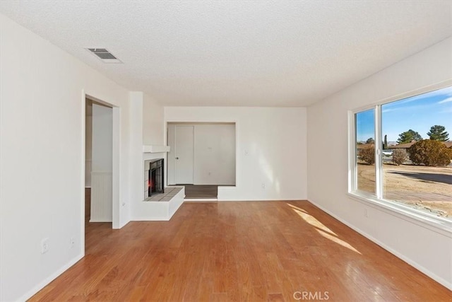 unfurnished living room featuring a tiled fireplace, light hardwood / wood-style flooring, and a textured ceiling