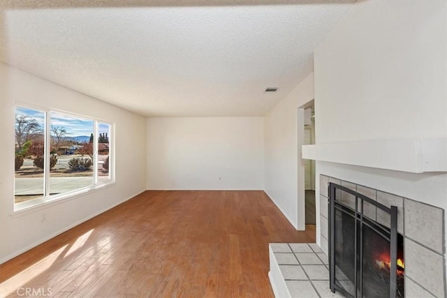 unfurnished living room featuring a tiled fireplace, a textured ceiling, and light wood-type flooring