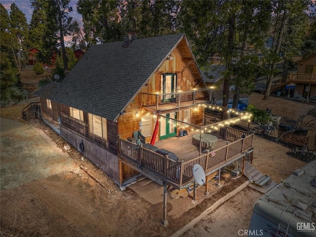 back house at dusk with a balcony and a wooden deck