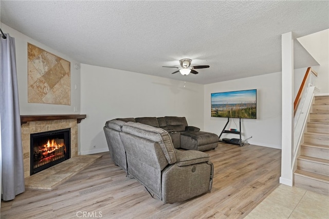 living room with light wood-type flooring, ceiling fan, a textured ceiling, and a tile fireplace