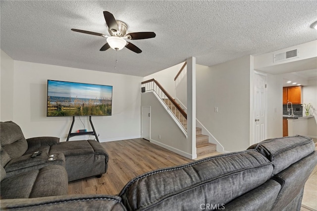 living room with a textured ceiling, ceiling fan, light hardwood / wood-style flooring, and sink