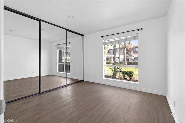 unfurnished bedroom featuring a closet, dark hardwood / wood-style flooring, and multiple windows