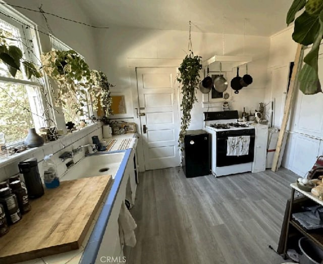 kitchen with wood-type flooring, sink, butcher block countertops, and white gas range oven