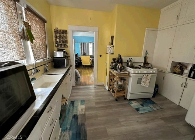 kitchen with hardwood / wood-style floors, gas range gas stove, sink, white cabinetry, and tile counters