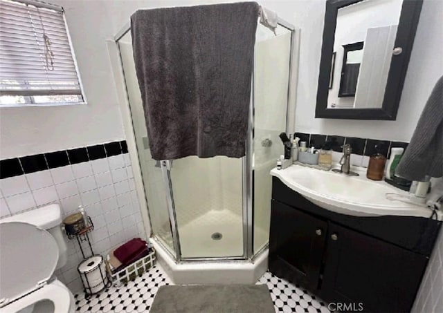 bathroom with tile patterned flooring, a shower with door, vanity, tile walls, and toilet