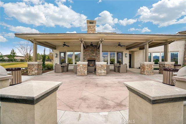 view of patio with an outdoor stone fireplace, ceiling fan, and exterior kitchen