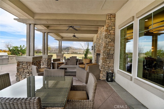 view of patio / terrace with grilling area, a mountain view, ceiling fan, and an outdoor stone fireplace