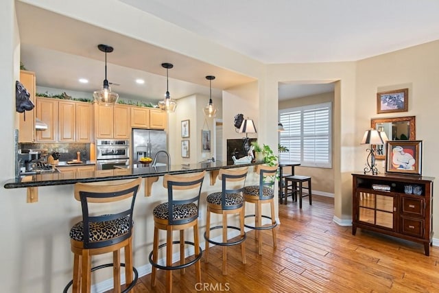 kitchen with stainless steel fridge with ice dispenser, backsplash, kitchen peninsula, pendant lighting, and light wood-type flooring