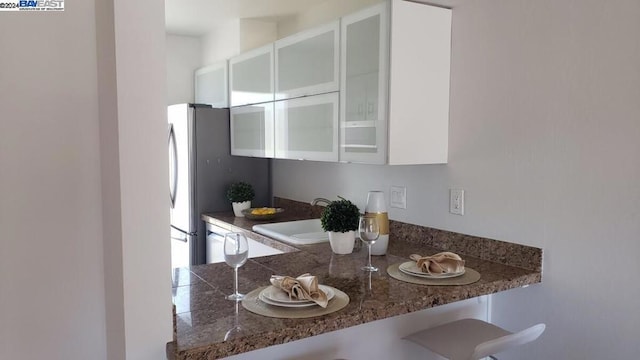 kitchen featuring white cabinets, a kitchen bar, sink, kitchen peninsula, and stainless steel refrigerator