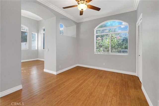 empty room with ceiling fan, a wealth of natural light, ornamental molding, and hardwood / wood-style floors