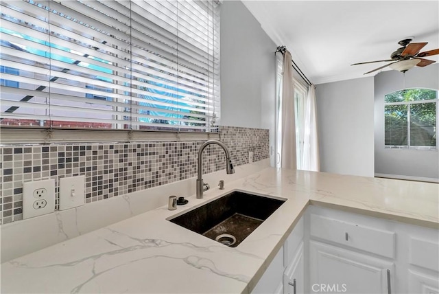 kitchen with light stone counters, sink, white cabinetry, and ceiling fan