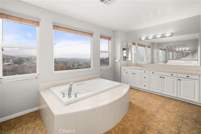 bathroom featuring vanity, tile patterned flooring, a healthy amount of sunlight, and tiled tub