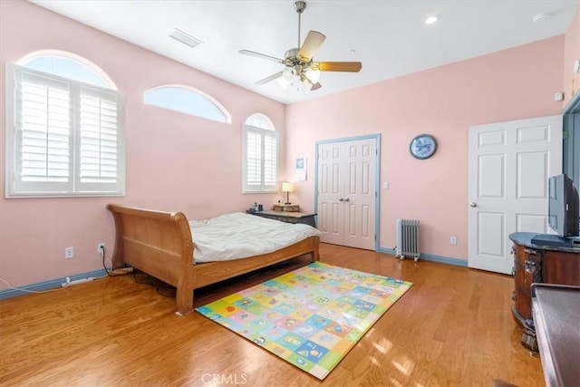 bedroom with ceiling fan, radiator heating unit, a closet, and light hardwood / wood-style flooring