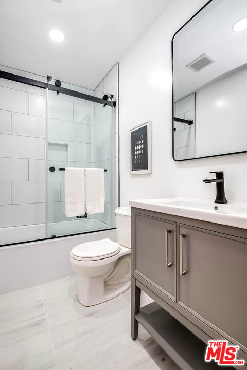 full bathroom featuring toilet, vanity, and shower / bath combination with glass door