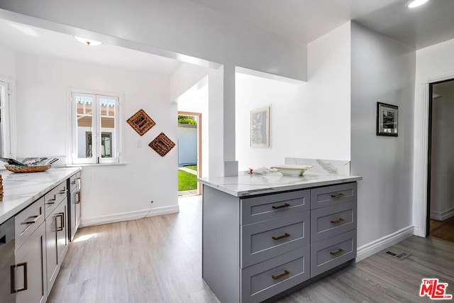 kitchen featuring kitchen peninsula, light wood-type flooring, light stone countertops, and gray cabinetry