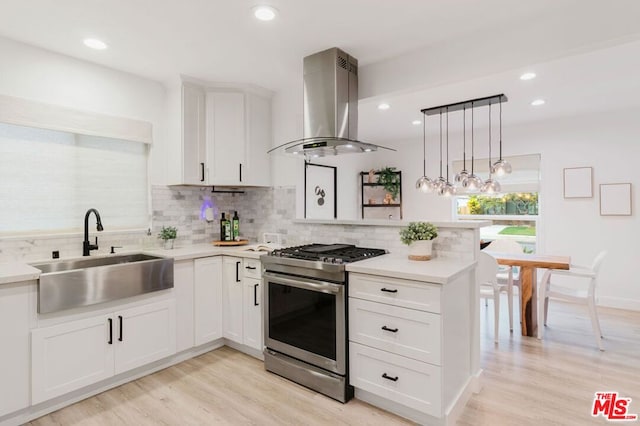 kitchen featuring stainless steel range with gas cooktop, pendant lighting, island exhaust hood, white cabinets, and sink