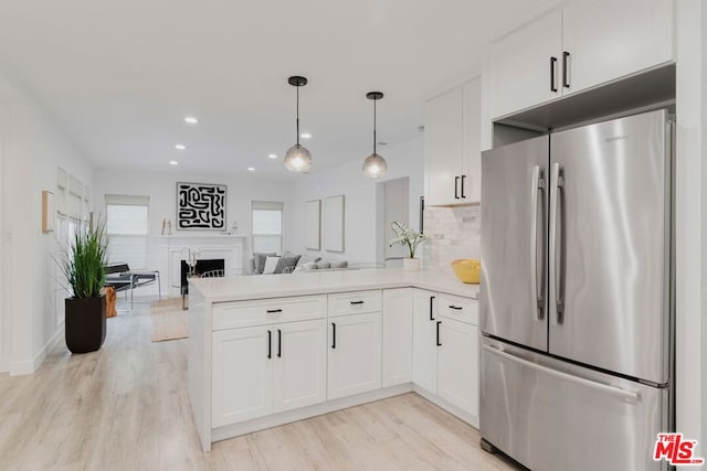 kitchen with stainless steel refrigerator, hanging light fixtures, kitchen peninsula, white cabinets, and light hardwood / wood-style flooring