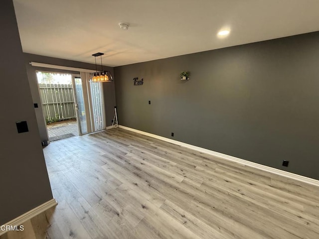 empty room with light wood-type flooring and a notable chandelier