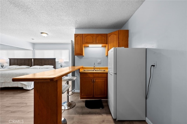 kitchen with a kitchen bar, sink, wood-type flooring, and white fridge