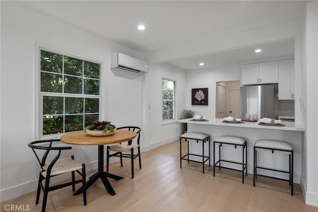 kitchen featuring stainless steel fridge, a wall unit AC, a breakfast bar area, tasteful backsplash, and white cabinets