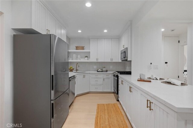 kitchen featuring white cabinets, stainless steel appliances, light hardwood / wood-style floors, sink, and decorative backsplash