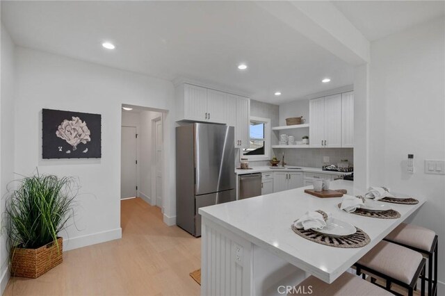 kitchen with decorative backsplash, appliances with stainless steel finishes, a kitchen breakfast bar, and white cabinetry