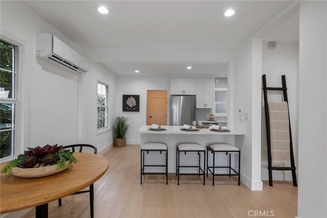 kitchen featuring an AC wall unit, white cabinetry, a kitchen breakfast bar, kitchen peninsula, and stainless steel refrigerator