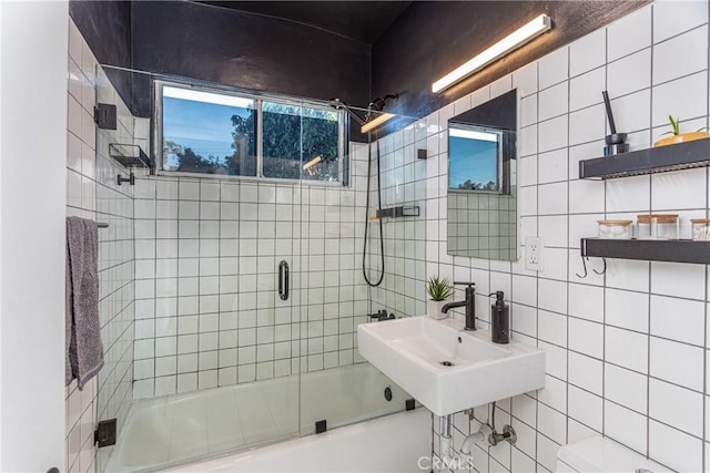 full bathroom featuring shower / bath combination with glass door, tasteful backsplash, sink, tile walls, and toilet