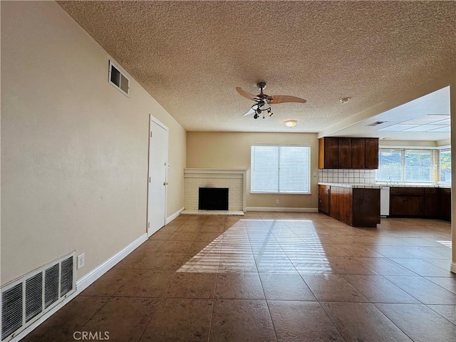 unfurnished living room featuring a textured ceiling, a brick fireplace, plenty of natural light, and ceiling fan