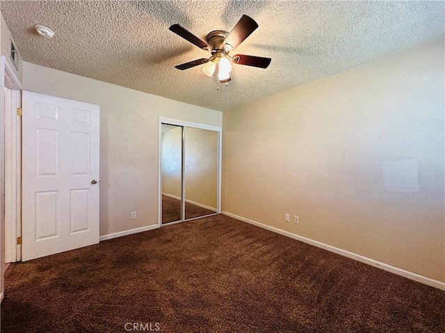 unfurnished bedroom featuring ceiling fan, a closet, a textured ceiling, and dark colored carpet