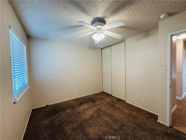 unfurnished bedroom featuring ceiling fan, a closet, a textured ceiling, and dark colored carpet