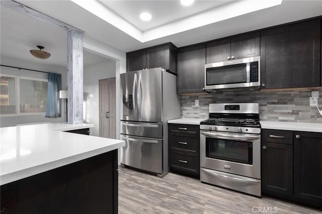 kitchen featuring decorative backsplash, a tray ceiling, stainless steel appliances, and light hardwood / wood-style flooring