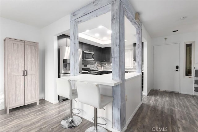 kitchen with dark wood-type flooring, stainless steel appliances, a kitchen breakfast bar, backsplash, and kitchen peninsula