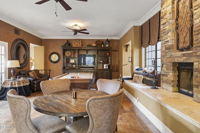 dining area with ceiling fan, hardwood / wood-style floors, a stone fireplace, ornamental molding, and pool table