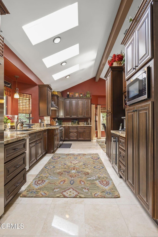 kitchen with vaulted ceiling with skylight, pendant lighting, dark brown cabinetry, light stone countertops, and dishwashing machine