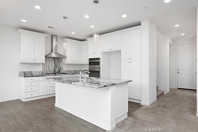 kitchen with pendant lighting, dark stone countertops, white cabinetry, and wall chimney exhaust hood