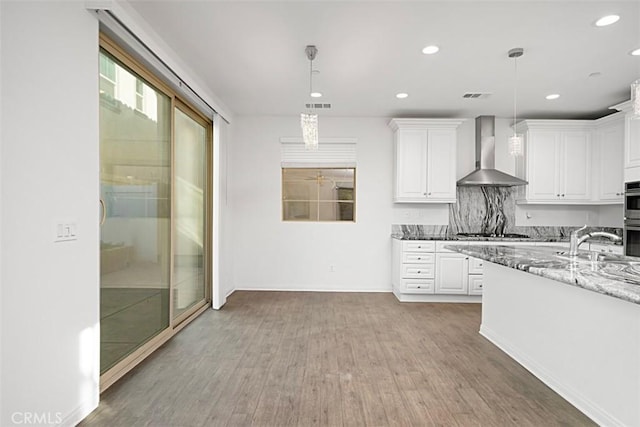 kitchen with light stone countertops, pendant lighting, white cabinets, wall chimney exhaust hood, and decorative backsplash