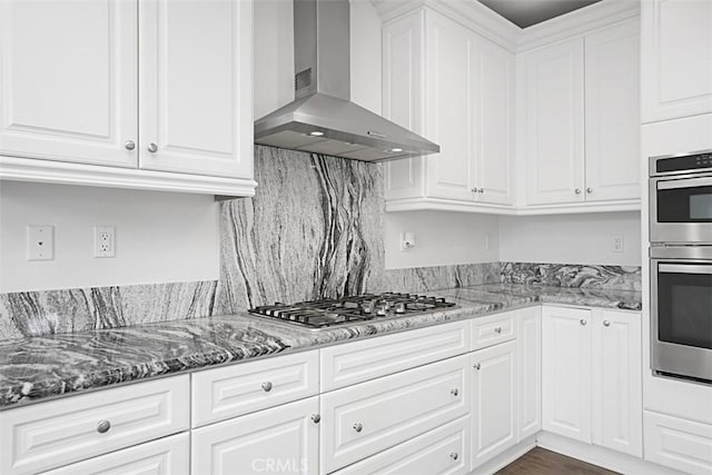 kitchen with stainless steel appliances, white cabinetry, dark stone counters, and wall chimney exhaust hood