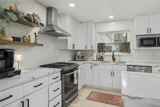 kitchen with stainless steel appliances, wall chimney exhaust hood, white cabinetry, and sink