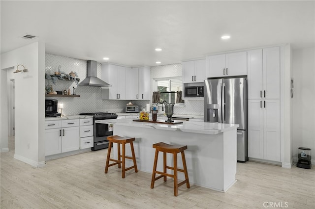 kitchen featuring white cabinetry, stainless steel appliances, a kitchen breakfast bar, wall chimney range hood, and a kitchen island