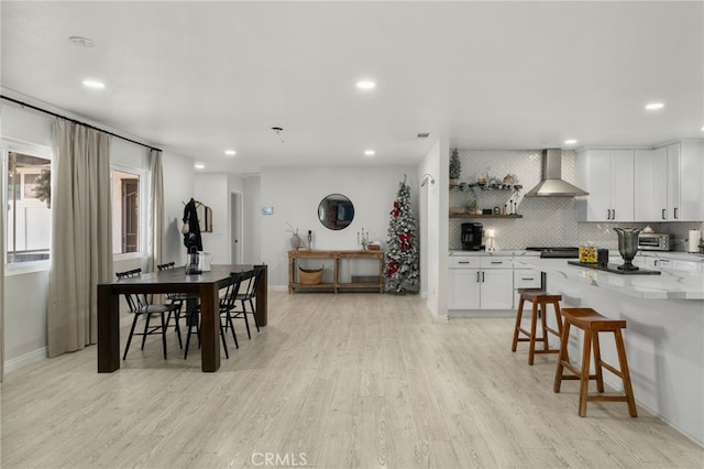 kitchen with backsplash, light hardwood / wood-style floors, a kitchen breakfast bar, white cabinets, and wall chimney exhaust hood