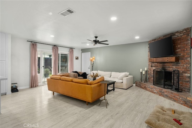 living room with light wood-type flooring, ceiling fan, and a fireplace