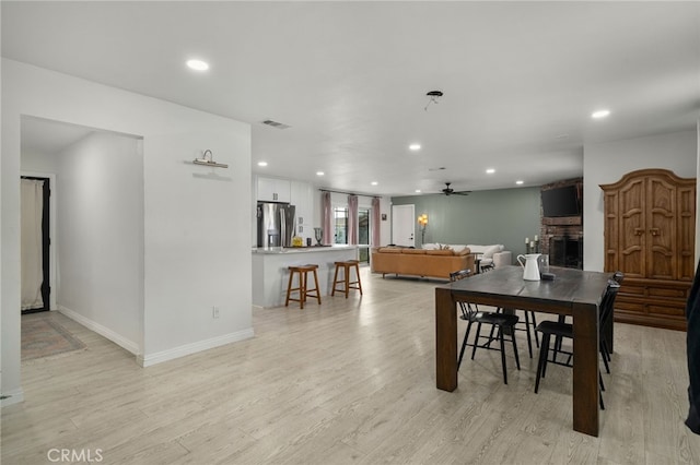 dining space with ceiling fan, a fireplace, and light hardwood / wood-style flooring