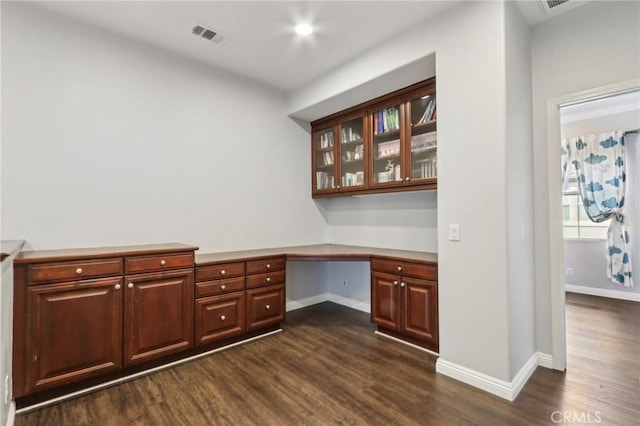 unfurnished office featuring built in desk and dark hardwood / wood-style floors