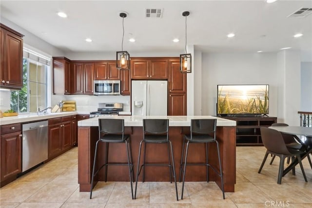 kitchen featuring light tile patterned floors, appliances with stainless steel finishes, hanging light fixtures, and a center island