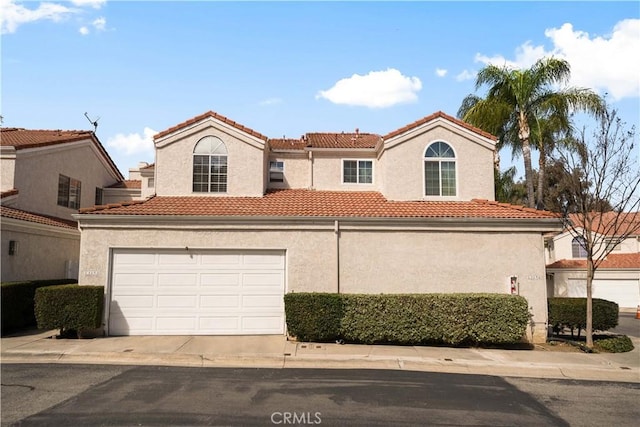 mediterranean / spanish-style home featuring a garage, a tiled roof, and stucco siding